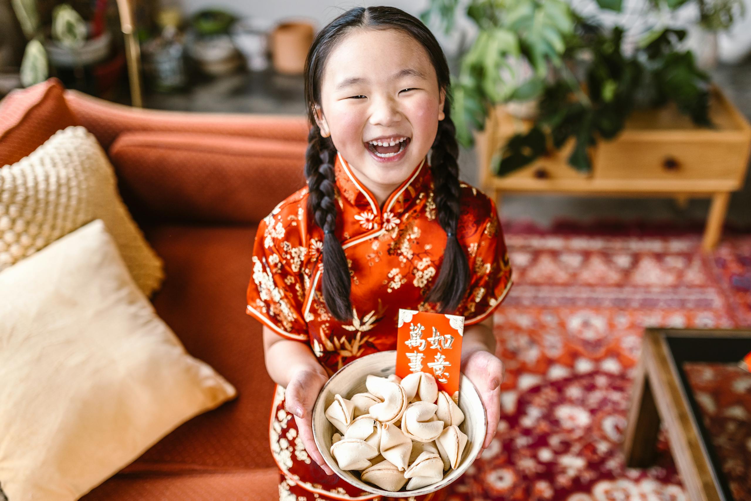 A smiling girl in a red cheongsam holds fortune cookies, celebrating Chinese New Year.
